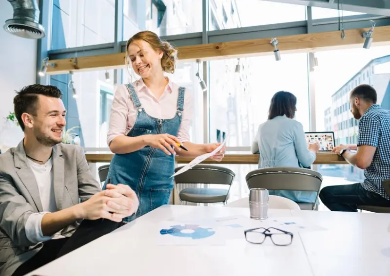 Team collaborating in bright workspace around table sharing papers and laptops near window light business directory